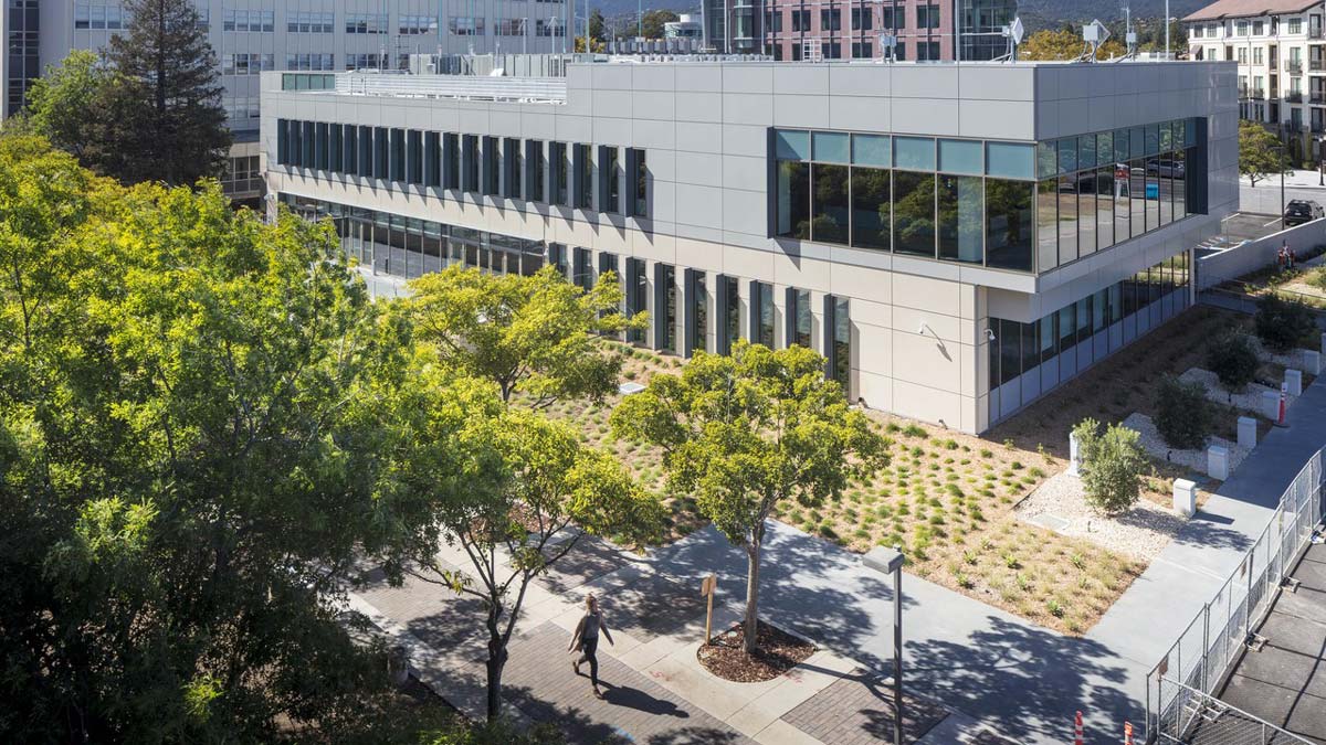 San Mateo County Regional Operations Center, a modern two-story building with landscaped garden, viewed from above with trees and pedestrian walkway in foreground