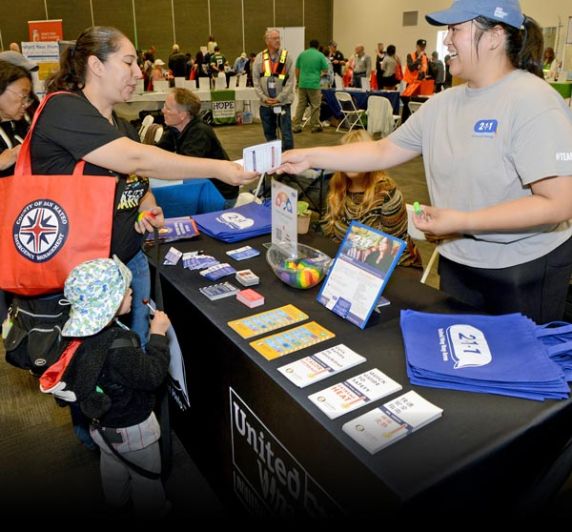 211 volunteer hands out information cards to a woman and a child