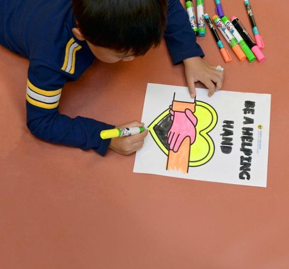 child coloring a Be a Helping Hand poster with markers during community art activity