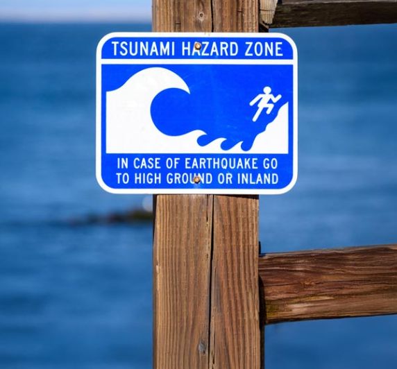 tsunami hazard zone sign near ocean, advising evacuation to high ground after earthquake