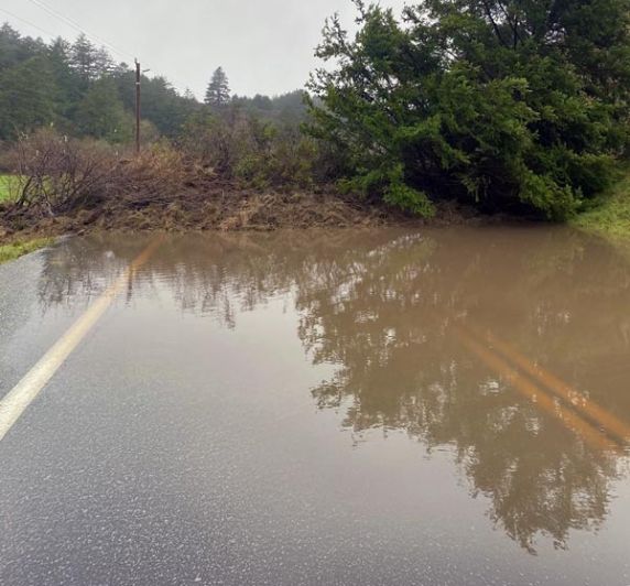 flooded rural road with fallen tree and debris near Cloverdale Road after heavy rain