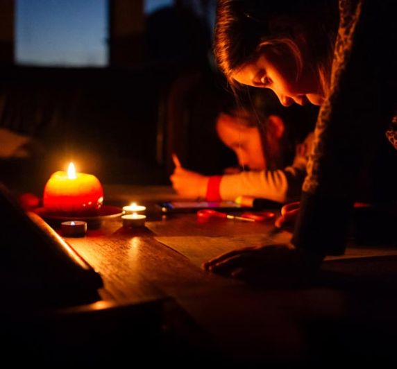 two little girls draw on a table with a candle during a power outage