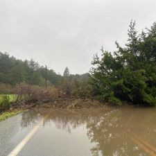 flooded rural road with fallen tree and debris near Cloverdale Road after heavy rain