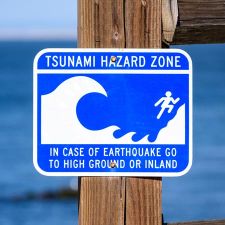 tsunami hazard zone sign near ocean, advising evacuation to high ground after earthquake