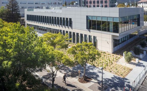 San Mateo County Regional Operations Center, a modern two-story building with landscaped garden, viewed from above with trees and pedestrian walkway in foreground