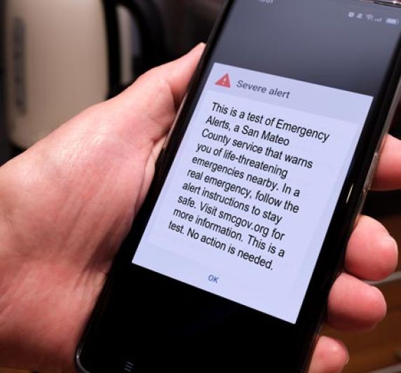 closeup of person holding phone displaying San Mateo County test of emergency alerts